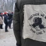 A person's back with large patch on their jacket that says, "Together we will stop line 3 (Kill the black snake)."