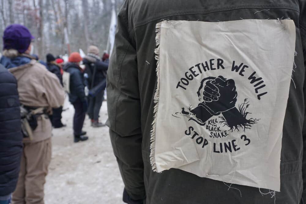 A person's back with large patch on their jacket that says, "Together we will stop line 3 (Kill the black snake)."
