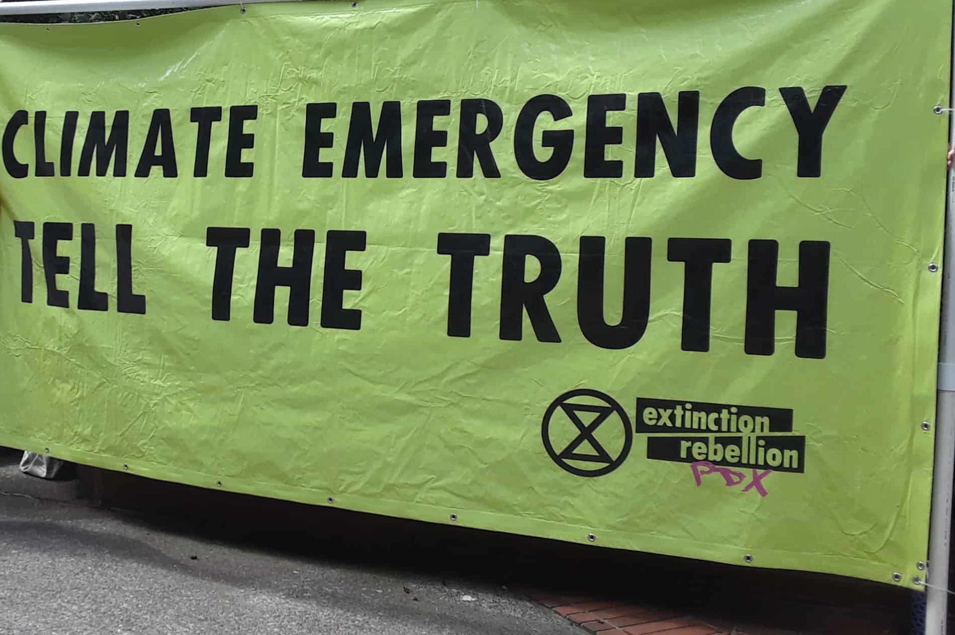Two people standing next to a big green banner that says "Climate Emergency: Tell the Truth"