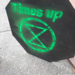 A black cardboard sign with day-glo green spray paint lettering. It says "Times up" with an XR logo under it.