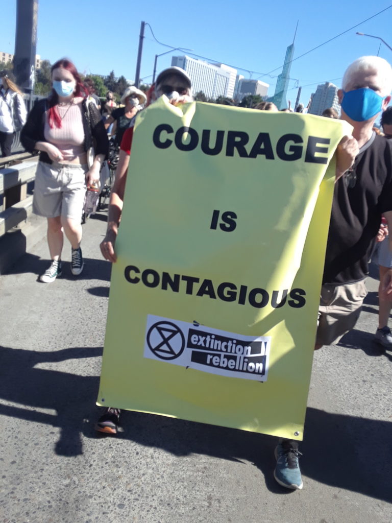 Vertical banner reading "Courage Is Contagious" with Extinction Rebellion logo at bottom.