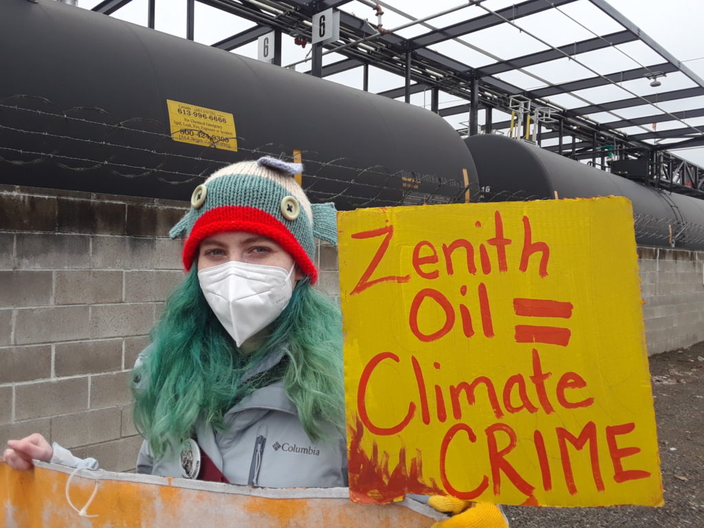 Youth climate activist holding sign saying "Zenith Oil = Climate Crime"