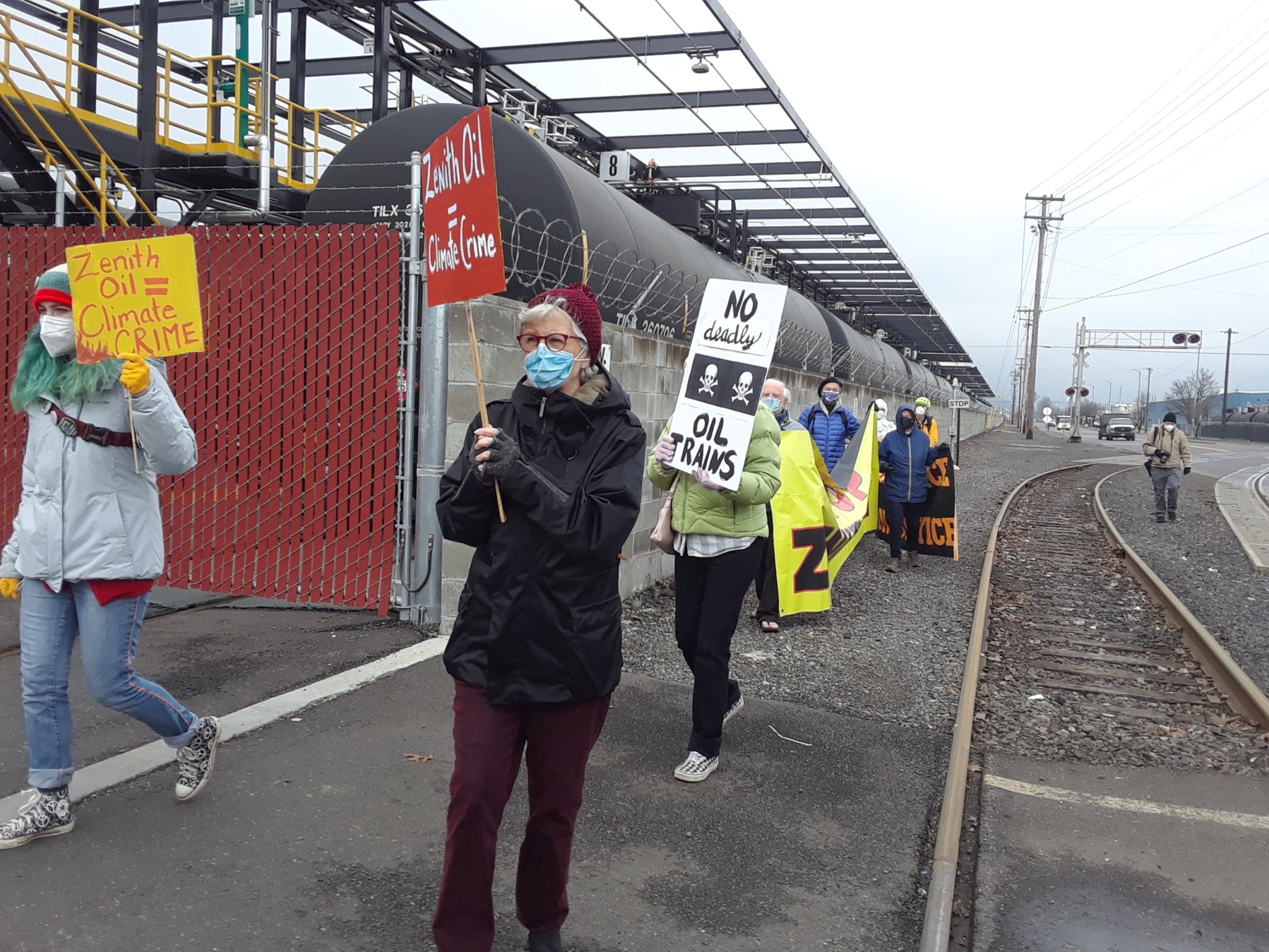 A line of protesters carrying signs and banners at the front gate of Zenith Energy in Portland, OR