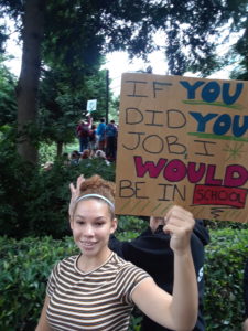 Girl holding a sign saying If you did your job I would be in school
