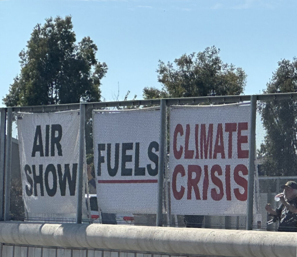 Three signs saying "Air Show/ Fuels/ Climate Crisis"